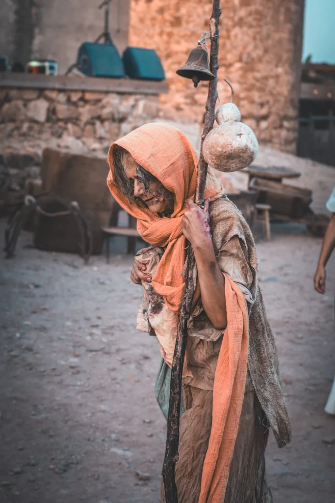 Person in medieval costume with a staff and rustic props during a historical re-enactment outdoors on an ancient site.
