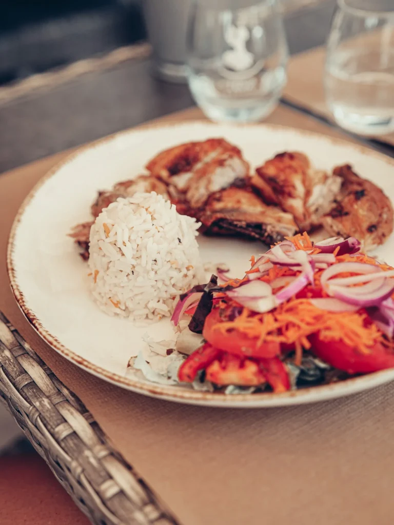 Roast chicken plate served with rice and a salad of raw vegetables, placed on a table at the Machado restaurant in Tavira, Algarve, early September 2026.