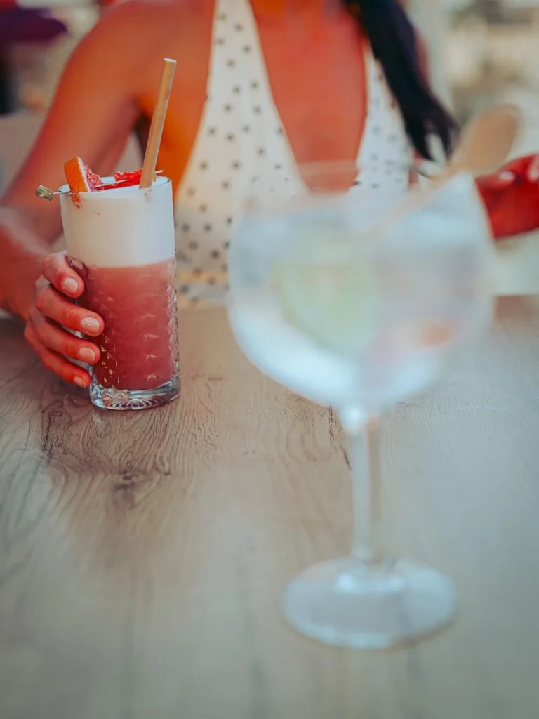 Caroline holds her Rooftop Gin on the terrace of Nomad in Tavira, Xavier's gin and tonic in the foreground: the two drinks from the evening of September 2, 2026.