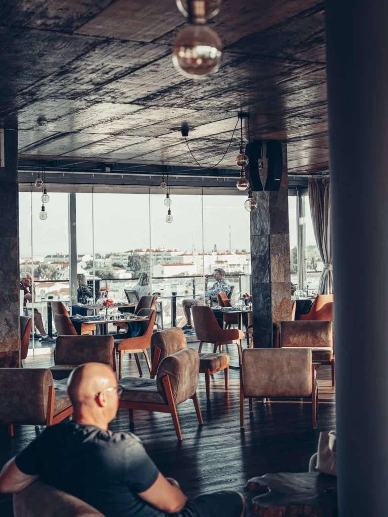 The interior space of the Nomad in Tavira: a wooden-furnished lounge widely open to the panorama through large bay windows, allowing you to enjoy the view even without being on the terrace.