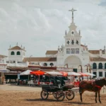 Horse-drawn carriage and white sanctuary beside the sandy square of El Rocío