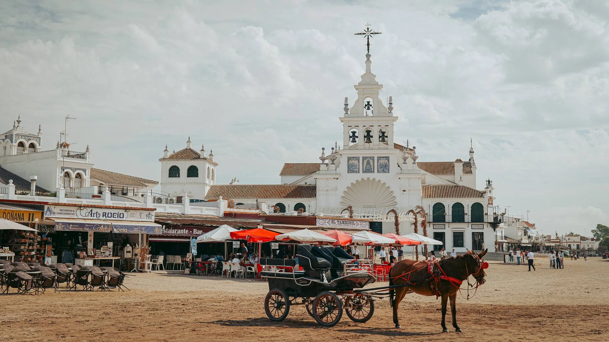 Horse-drawn carriage and white sanctuary beside the sandy square of El Rocío